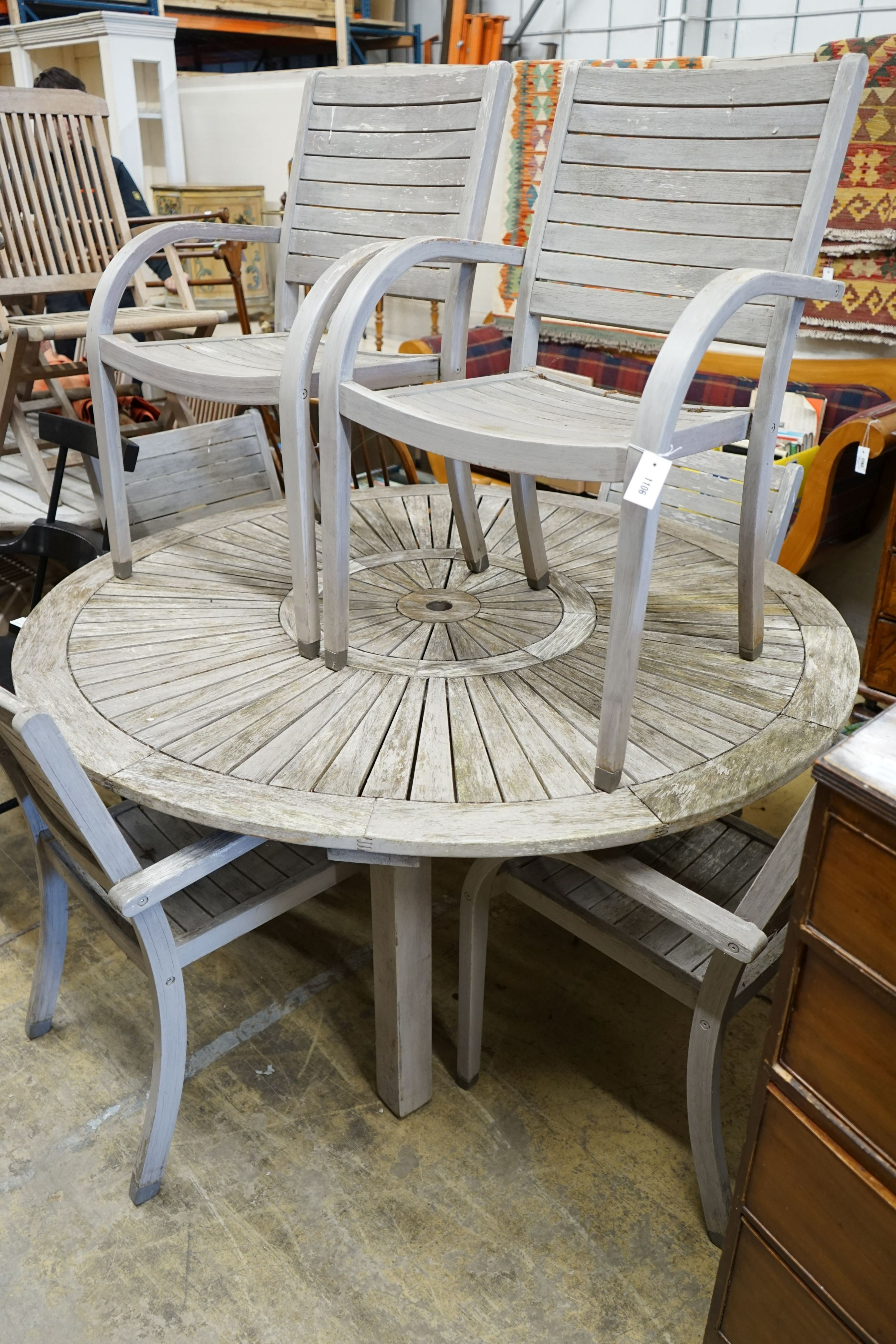 A circular weathered teak garden table, diameter 153cm, height 75cm together with six weathered teak stacking garden elbow chairs